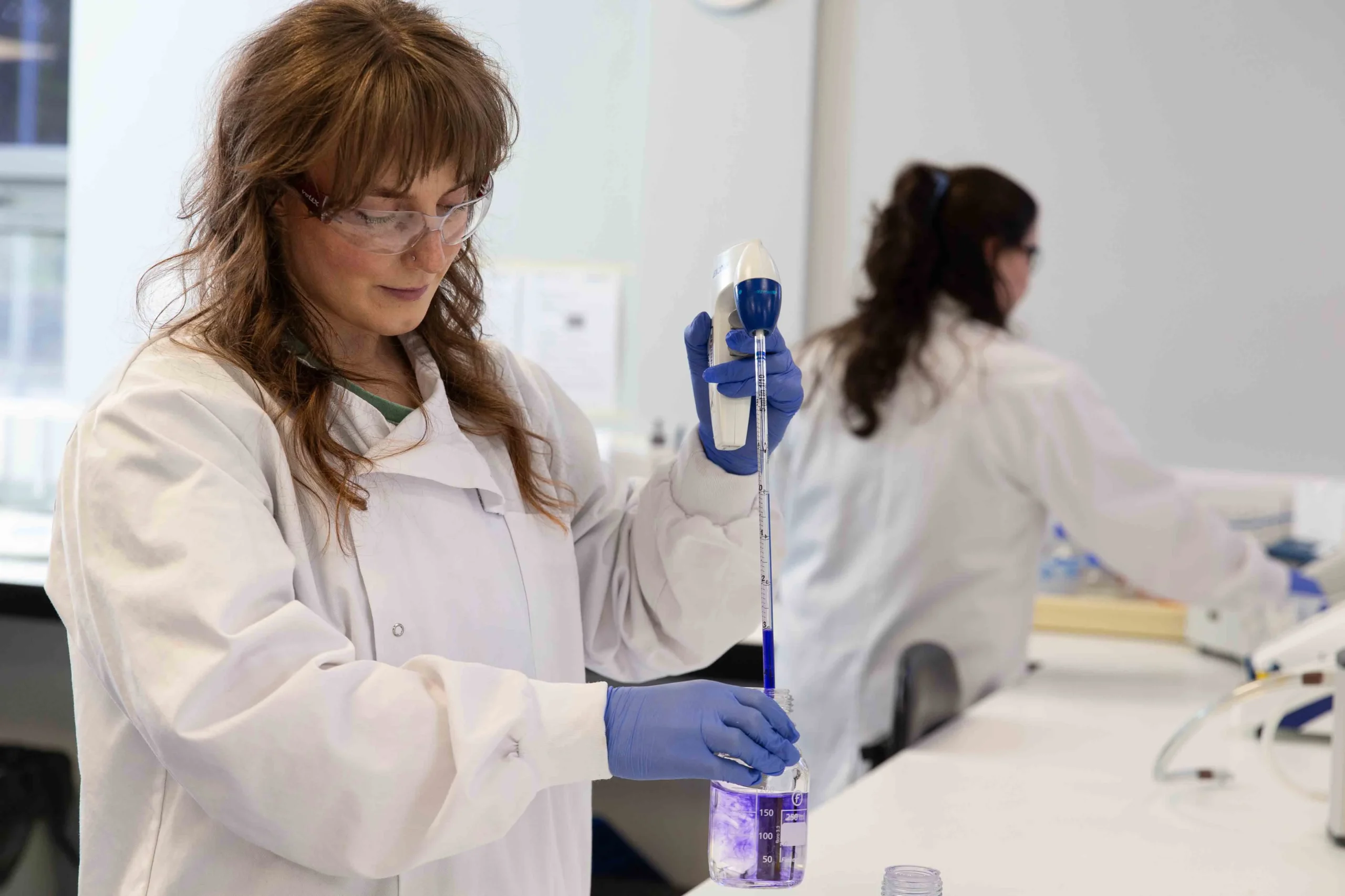 Scientist performing pipetting in a laboratory setting, representing custom assay development and advanced bioscience solutions for drug discovery.