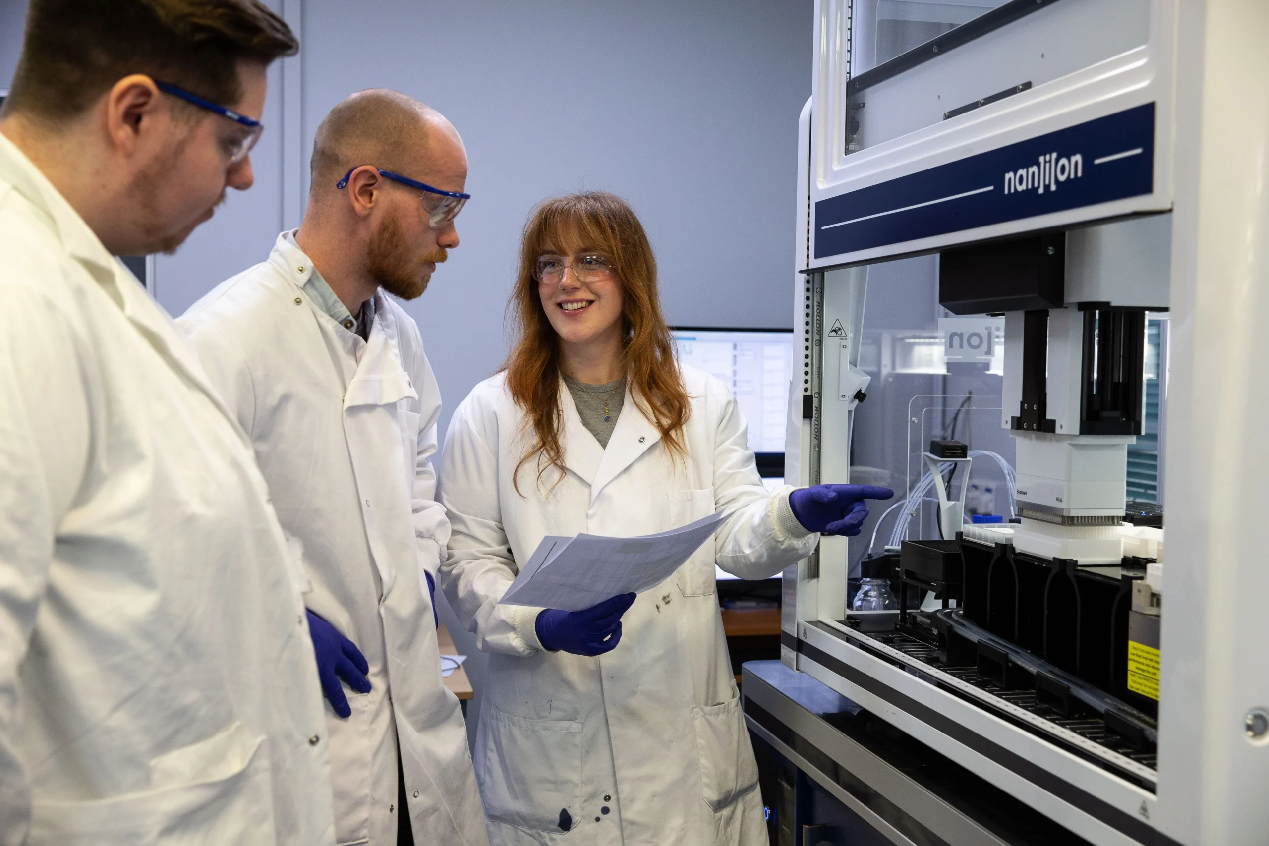 Laboratory setting with scientists reviewing data near an automated screening system, illustrating customized screening cascades for ion channel assay development and pharmacology workflows.