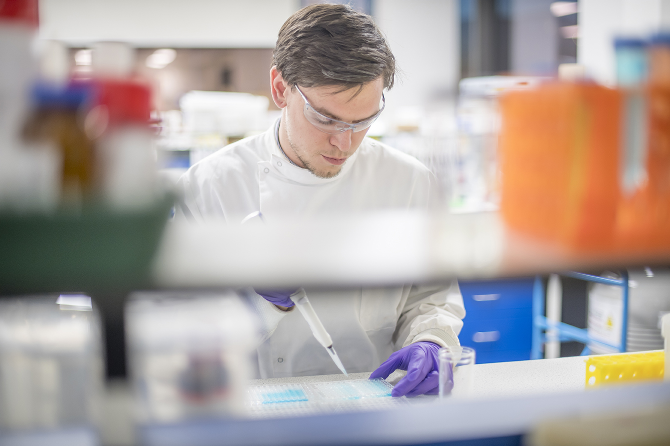 Laboratory setting with scientific equipment and colorful containers in the foreground, illustrating drug discovery workflows including assay development, high-throughput screening, and integrated pharmacology solutions.
