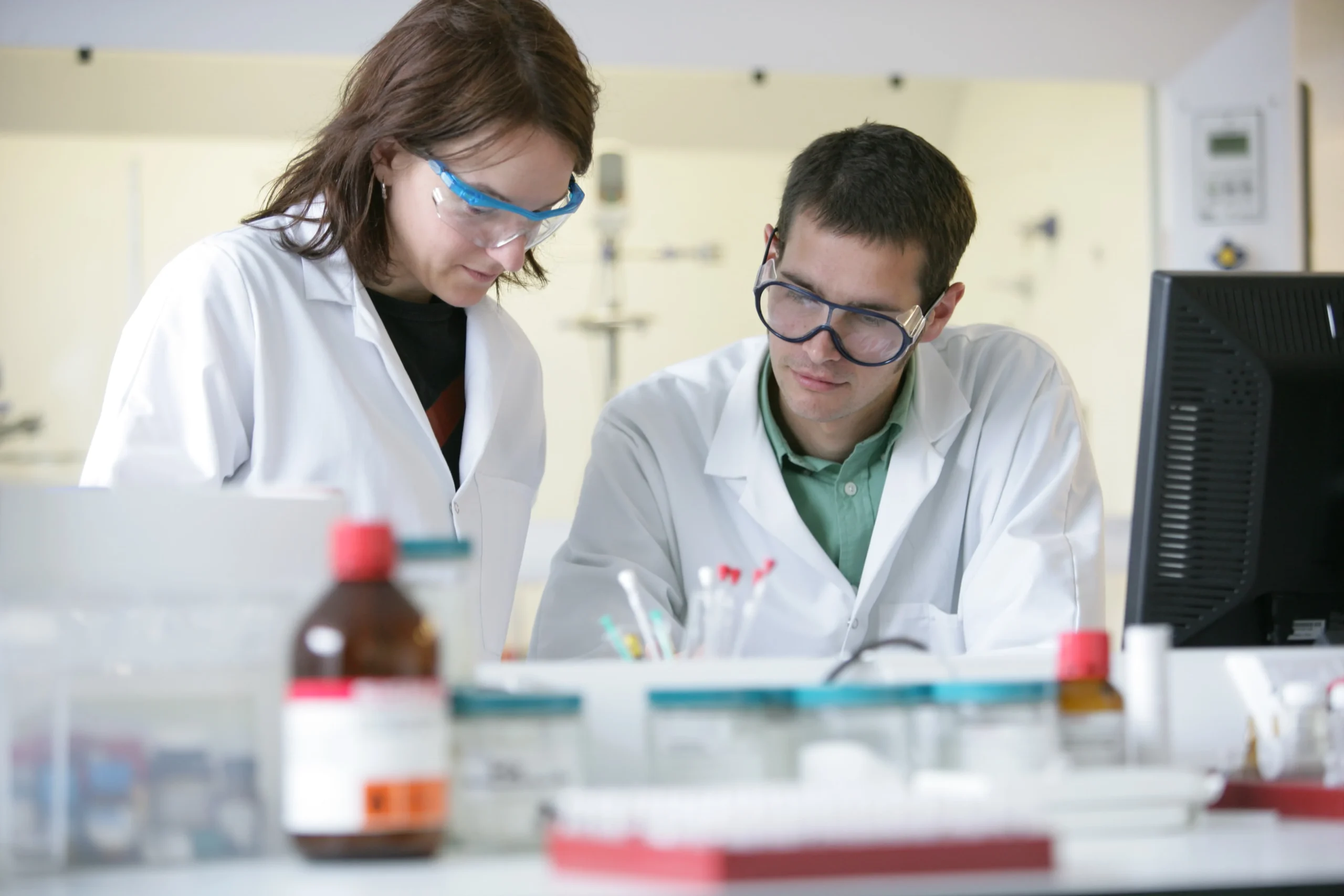 Laboratory setting showing scientists working with glassware and reagents, representing medicinal chemistry for optimizing drug profiles and advancing compounds toward clinical development.