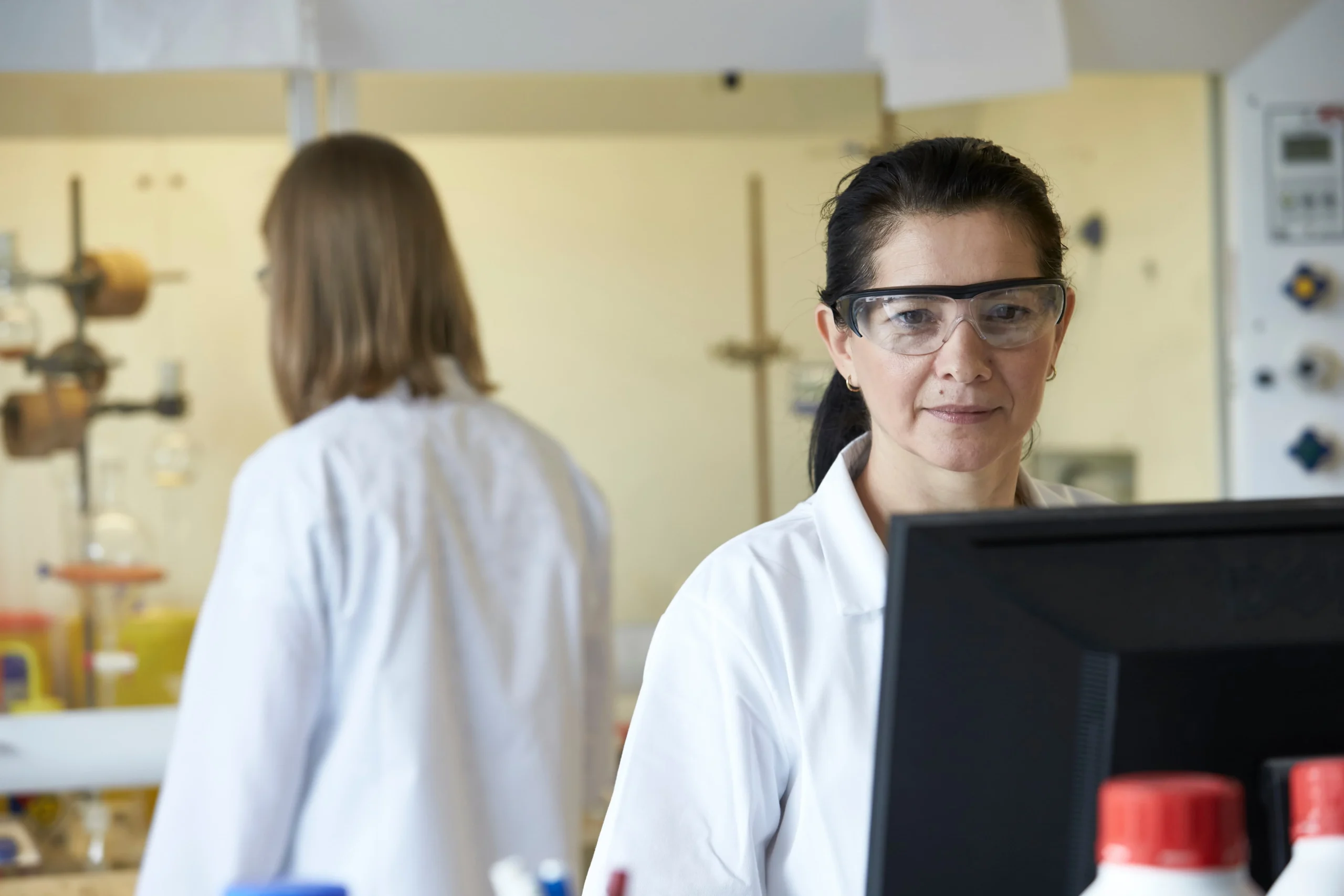 Laboratory environment with scientists working near a computer and chemical apparatus, representing physiologically based pharmacokinetic (PBPK) modelling for ADME simulation and regulatory planning in drug development.
