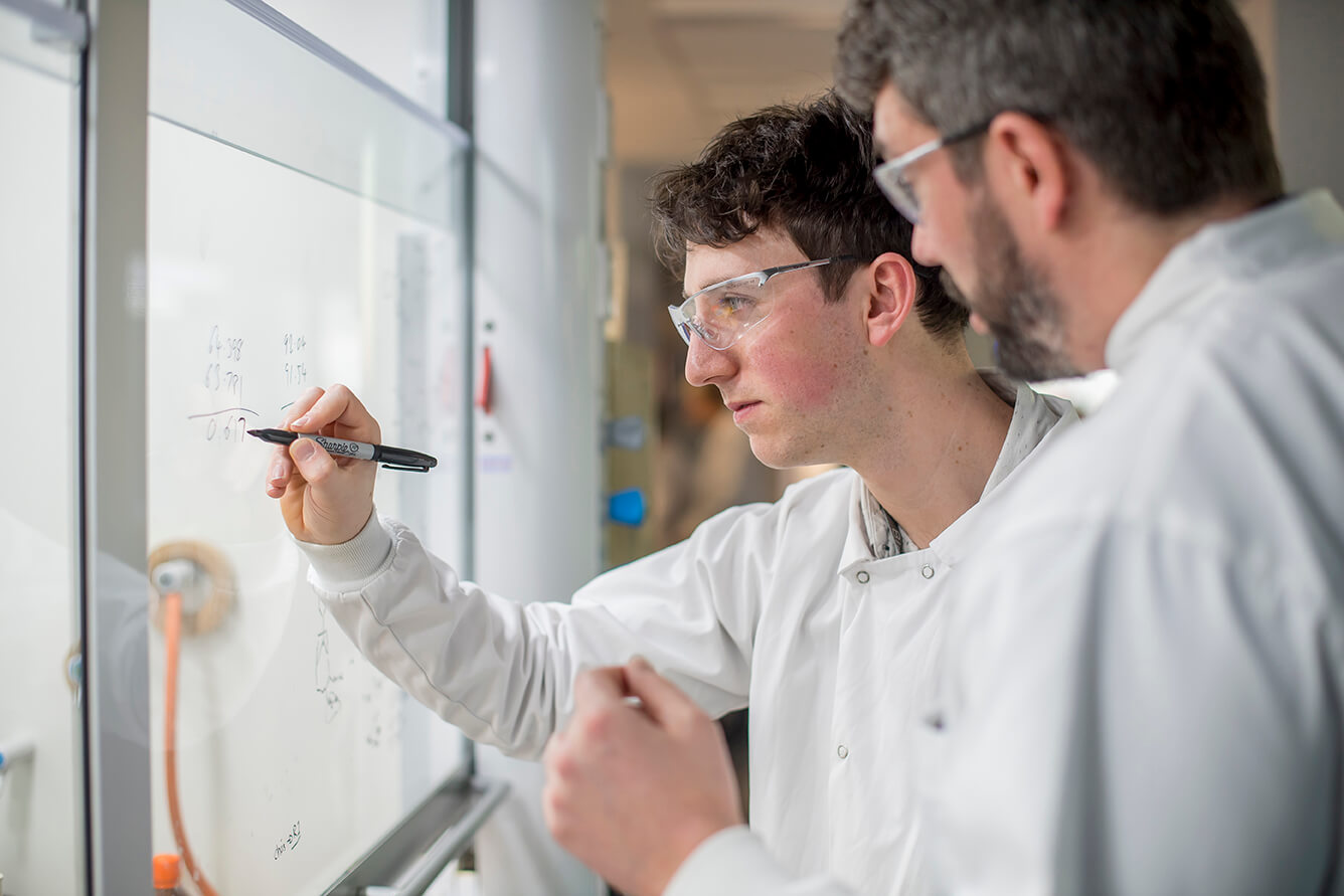 Researchers collaborating at a whiteboard in a laboratory environment, focusing on lead optimization to advance clinical candidates.